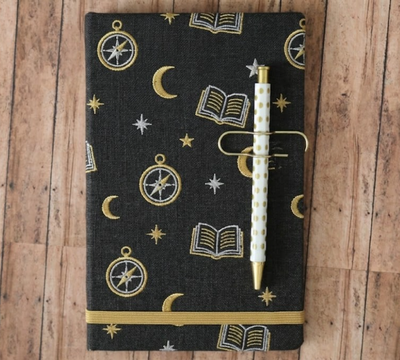 Black notebook with celestial pattern and pen on wooden surface